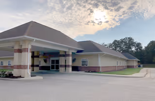 Exterior view of a single-story building with a covered entrance and a paved driveway under a partly cloudy sky.