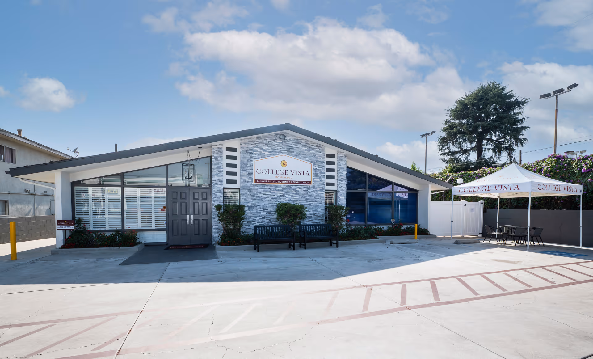 Exterior view of College Vista Post-Acute facility showing a single-story building with a slanted roof, large windows, a central entrance door, two benches in front, and a white canopy tent with College Vista branding on the right side. The area in front is a paved parking lot under a partly cloudy sky.