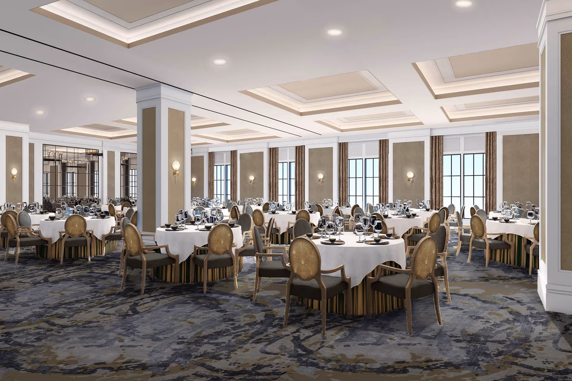 A spacious and elegant dining room with round tables covered in white tablecloths, each set with multiple wine glasses and black bowls. The room features large windows with brown curtains, beige walls with white trim, decorative wall sconces, and a patterned carpet in shades of blue and gray. The ceiling has recessed lighting and coffered design elements.