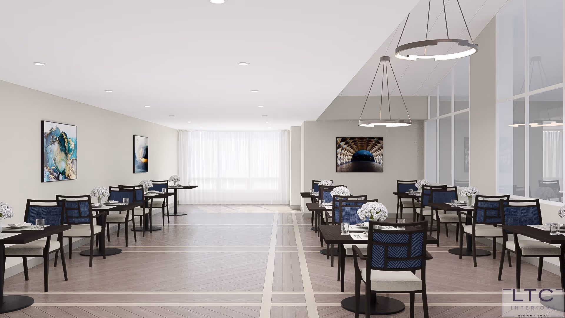 A bright and modern dining room with multiple dark wood tables and chairs arranged neatly. Each table has a small bouquet of white flowers and place settings. The room features light-colored walls with abstract artwork, large windows with sheer white curtains, and contemporary circular pendant lights hanging from the ceiling.