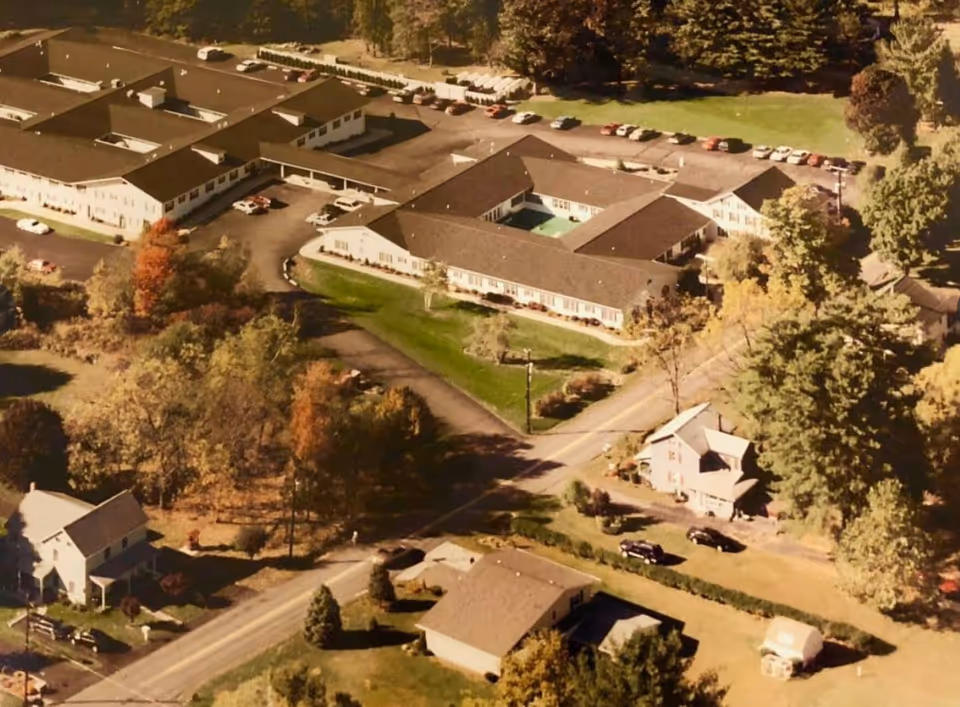 Aerial view of Fritzingertown Senior Living Community showing multiple single-story buildings with parking lots surrounded by trees and greenery in a suburban area.