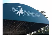 A green awning with white text and a logo that reads 'The Baptist Home at Brookmeade' with a silhouette of a person sitting on a bench holding an umbrella.