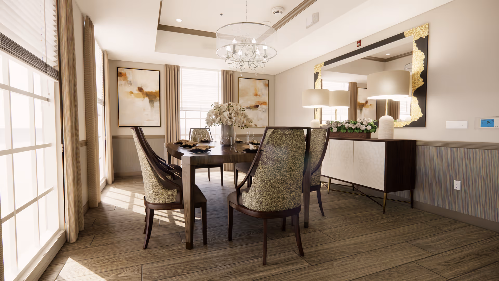 A bright dining room with a wooden dining table surrounded by six upholstered chairs. The table is set with plates and a vase of white flowers as a centerpiece. Large windows with beige curtains allow natural light to fill the room. On the wall opposite the windows, there is a large decorative mirror with gold accents above a sideboard that holds two lamps and a floral arrangement. Two abstract paintings hang on the wall between the windows.