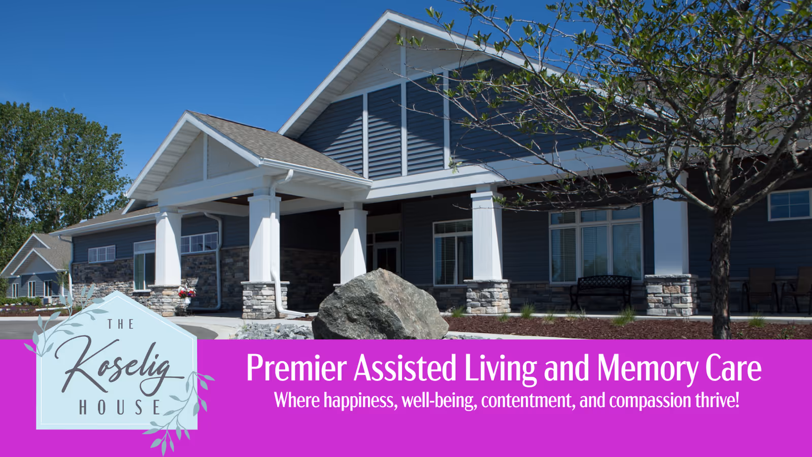 Exterior view of a single-story assisted living and memory care facility with a covered entrance, stone accents, and a tree in the foreground under a clear blue sky.