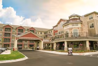 Exterior view of a senior living facility named New Perspective North Shore, showing a multi-story building with a covered entrance, balconies, and landscaped surroundings under a partly cloudy sky.