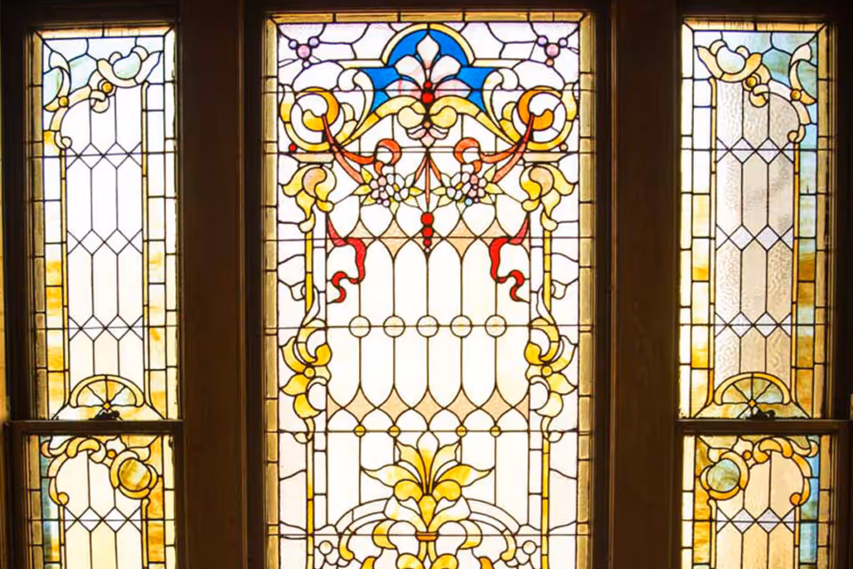 Decorative stained glass window with intricate patterns in yellow, red, blue, and white colors, featuring floral and geometric designs.