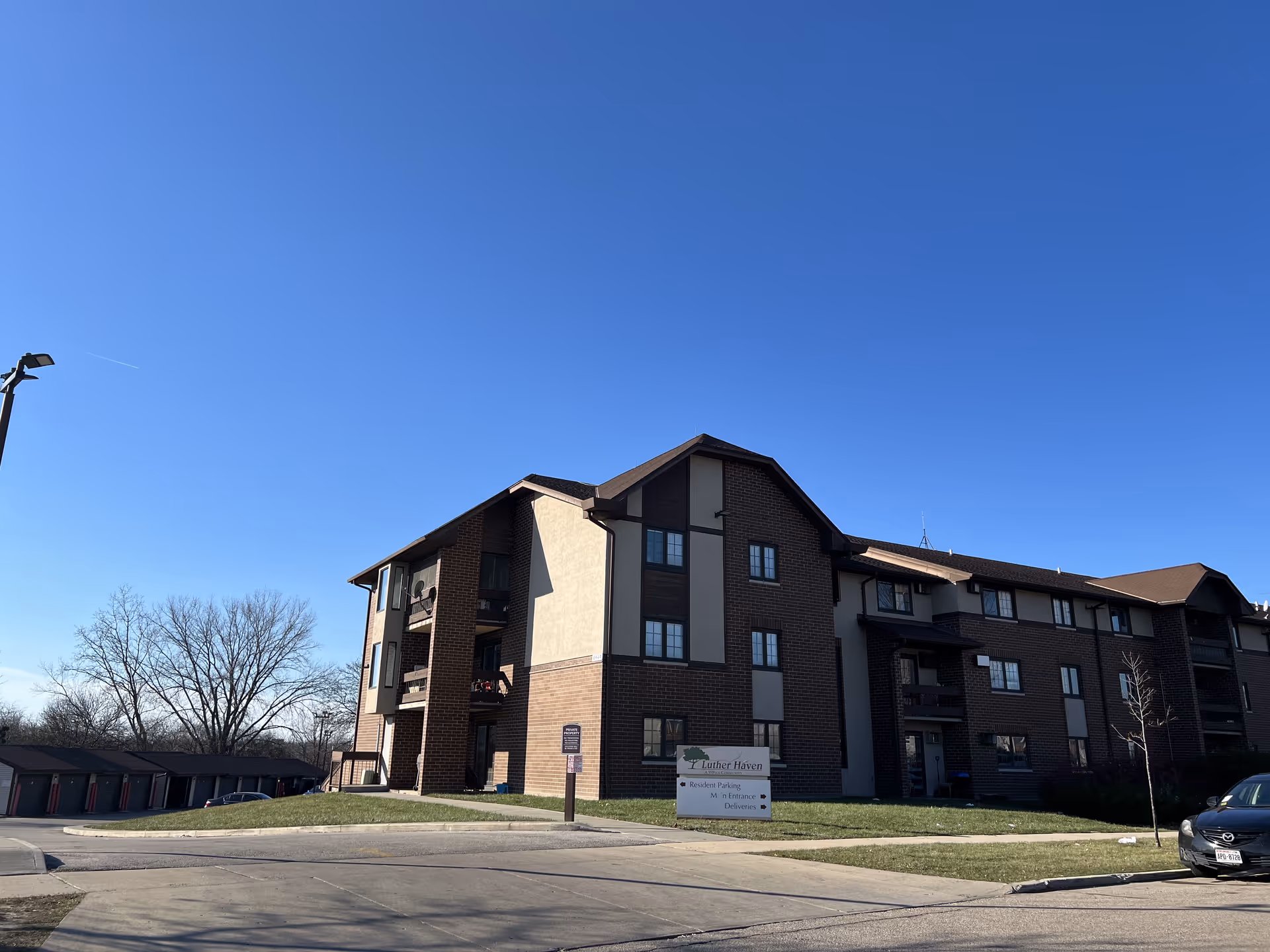 Exterior view of a multi-story senior living facility building named Luther Haven under a clear blue sky, with a parking area and some cars visible nearby.