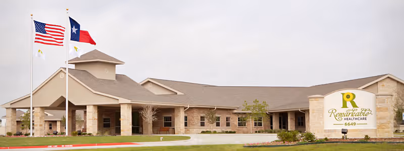 Exterior view of Remarkable Healthcare facility showing a single-story building with a covered entrance, three flagpoles with American, Texas, and facility flags, and a sign displaying the facility name and number 6649.