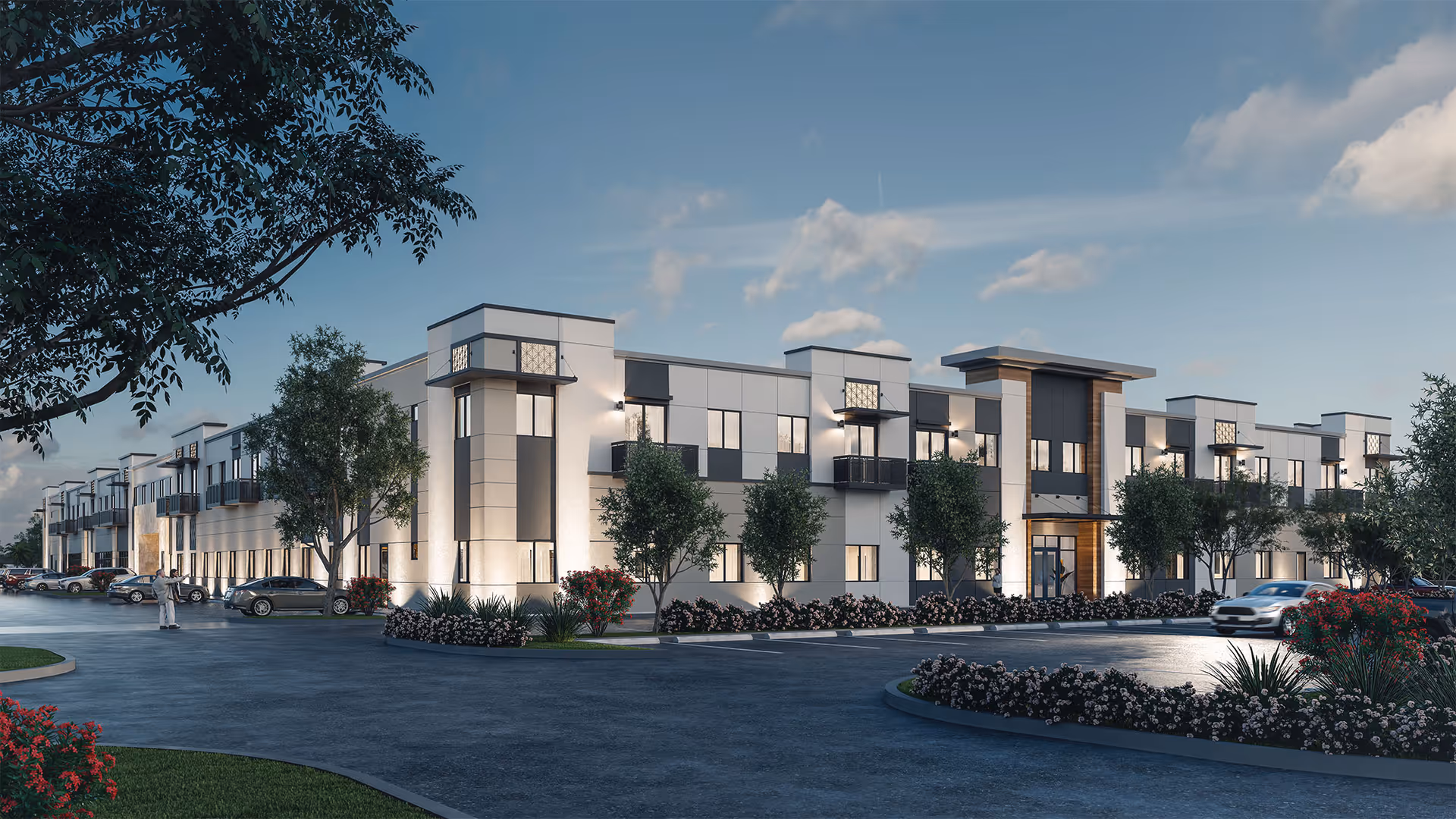 Exterior view of a modern two-story senior living facility building named The Contemporary Miami, with a parking lot in front, landscaped with trees and flowers, under a partly cloudy sky at dusk.
