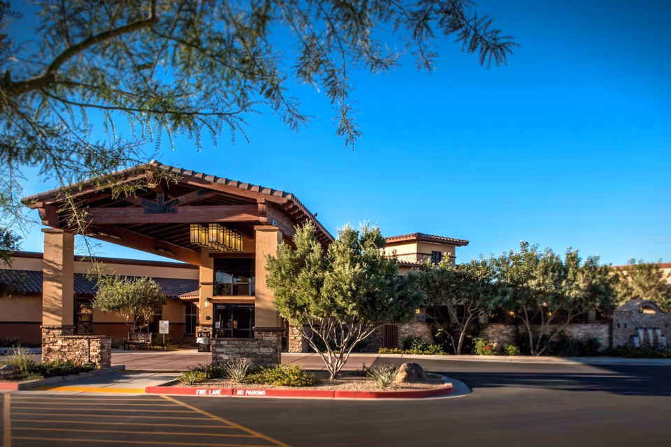 Exterior view of Santé of North Scottsdale - Skilled Nursing & Rehabilitation facility showing the main entrance with a covered driveway, surrounded by trees and landscaping under a clear blue sky.