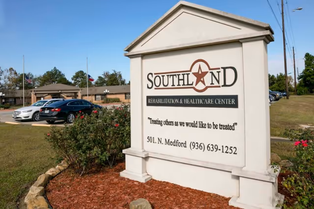 Outdoor view of the entrance sign for Southland Rehabilitation and Healthcare Center with a building and parked cars in the background under a clear blue sky.