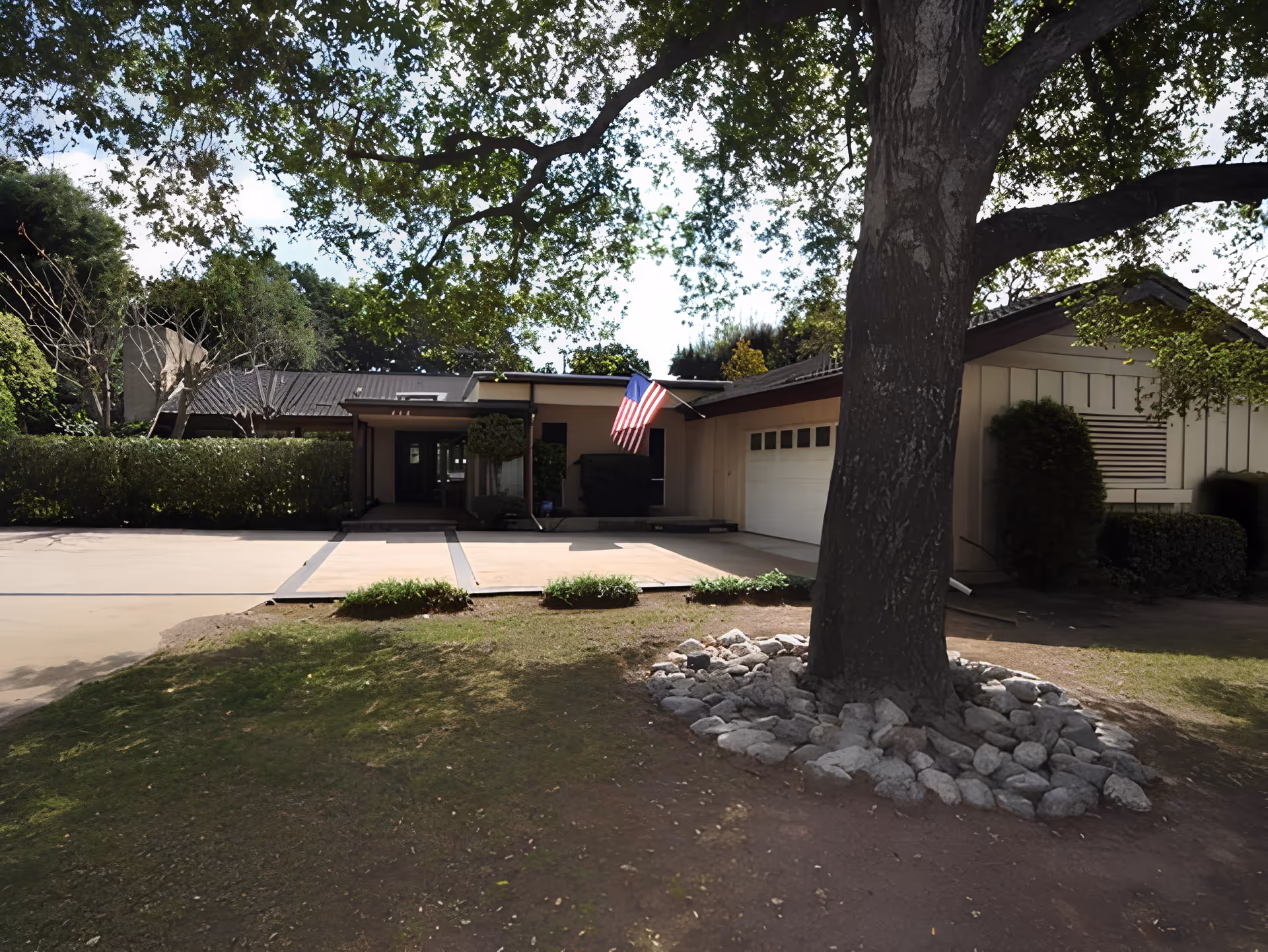 Front exterior view of a single-story building with a driveway, an American flag mounted near the entrance, surrounded by trees and bushes.