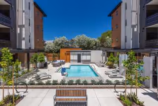 Outdoor courtyard area of Santana Terrace featuring a rectangular swimming pool surrounded by lounge chairs, greenery, and modern apartment buildings under a clear blue sky.