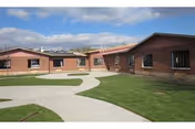 Outdoor view of a senior living facility named Generations at Applewood showing single-story brick buildings with multiple windows, a concrete walkway, and well-maintained green lawns under a partly cloudy sky.