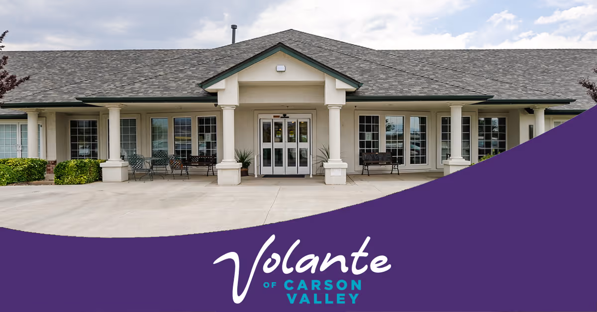 Front exterior view of Volante Senior Living of Carson Valley building with a covered entrance supported by columns, several windows, outdoor seating, and a paved driveway.