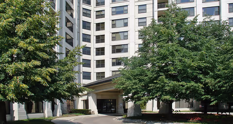 Exterior view of a multi-story senior living facility building with a covered entrance and large trees in front, located at Brookdale Des Plaines.