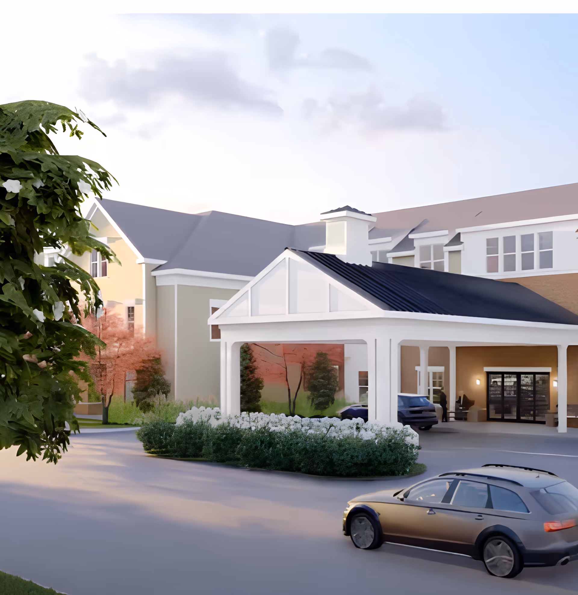 Exterior view of The Farmstead at Medford facility showing a covered entrance with white pillars, a driveway with a parked car, landscaped greenery including bushes and trees, and a multi-story building in the background under a partly cloudy sky.