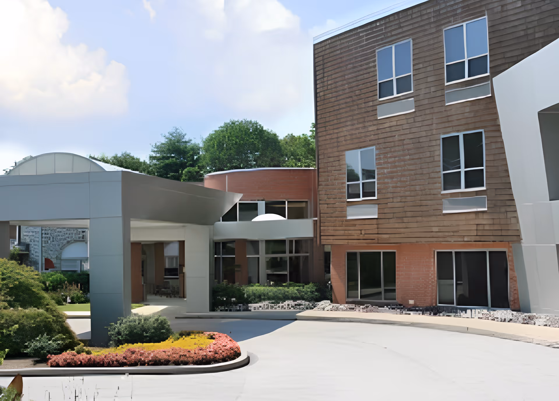 Exterior view of Springfield Crossings facility showing a modern building with large windows, a covered entrance, landscaped bushes, and a curved driveway under a partly cloudy sky.