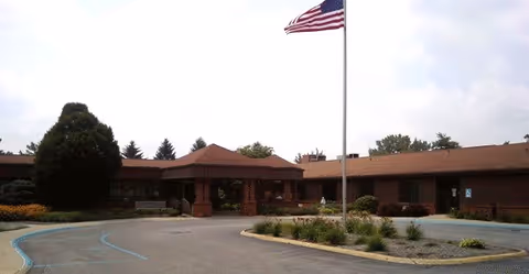 Exterior view of Cumberland Pointe Health Campus featuring a single-story building with a brown roof, a flagpole with an American flag in front, and a circular driveway with parking spaces.