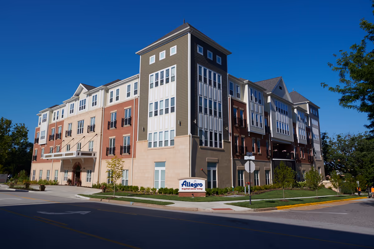 Exterior view of a multi-story senior living facility building named Allegro Senior Living – Richmond Heights, MO, with a clear blue sky and surrounding greenery.