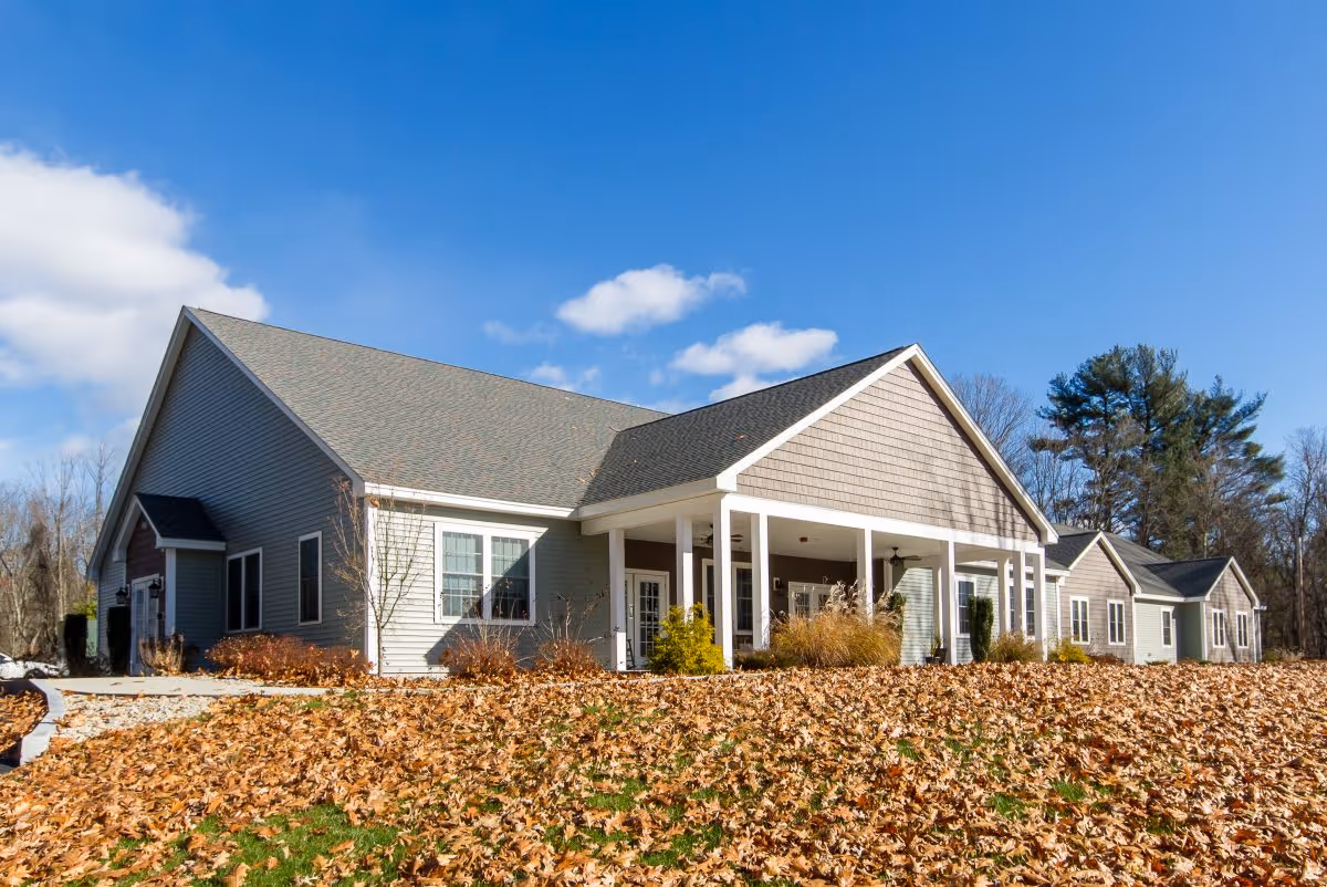 Exterior view of Beaver Lake Lodge Assisted Living building on a clear day with blue sky, surrounded by fallen autumn leaves and some trees in the background.