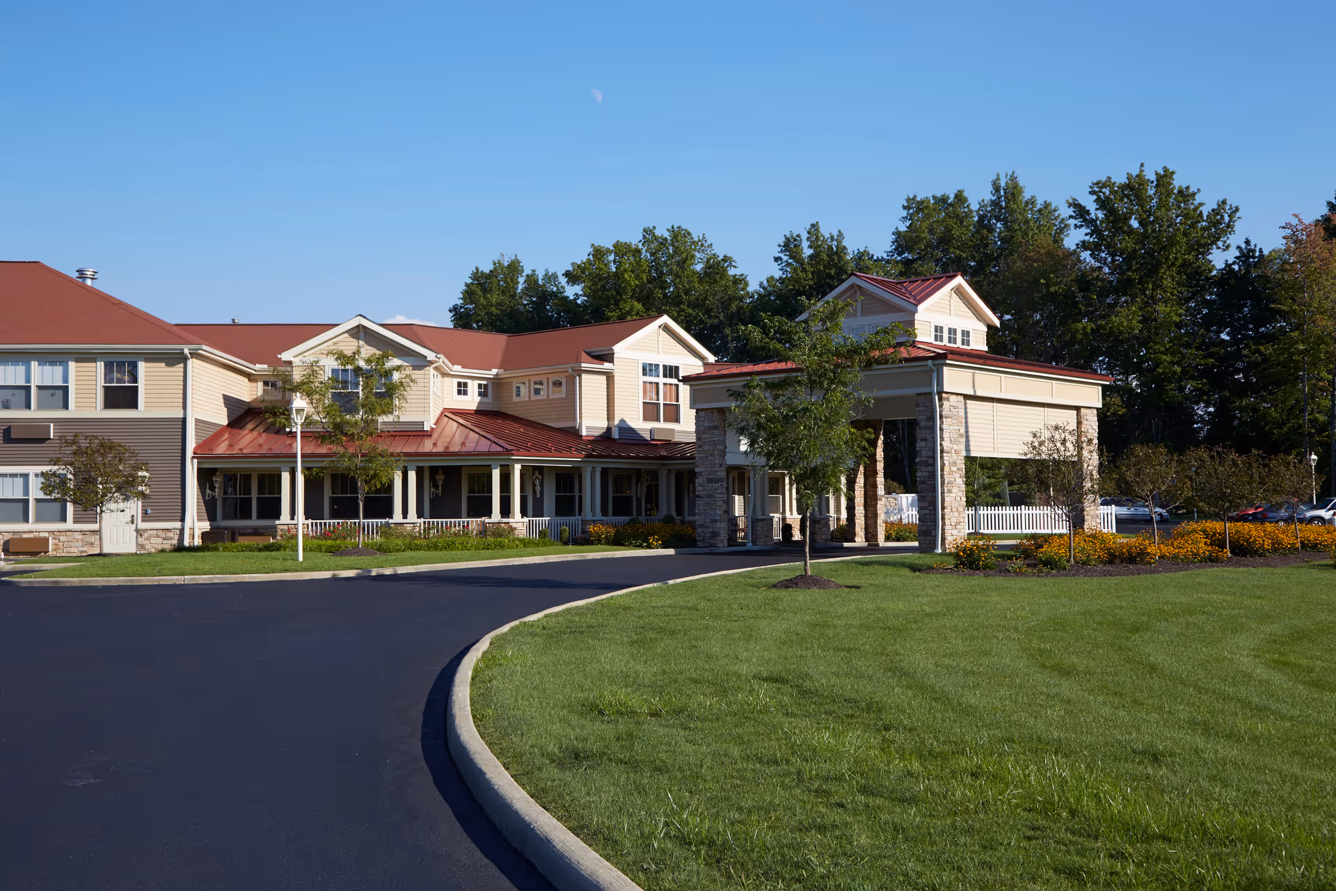 Exterior view of Aberdeen Crossings by New Perspective, showing a large building with beige siding and red roofs, surrounded by green grass, trees, and a paved driveway under a clear blue sky.