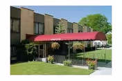 Exterior view of a two-story building with a red awning over the entrance, surrounded by green grass and trees under a clear blue sky.