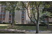 Exterior view of a multi-story residential building with several windows, surrounded by trees and a grassy lawn in front.