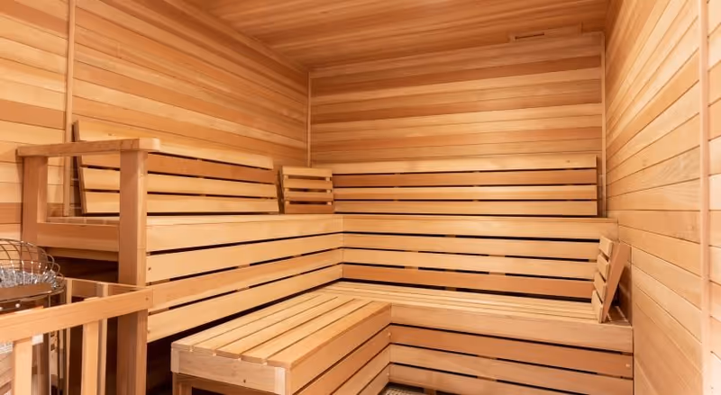 Interior view of a wooden sauna room with tiered wooden benches along the walls and a sauna heater in the corner.